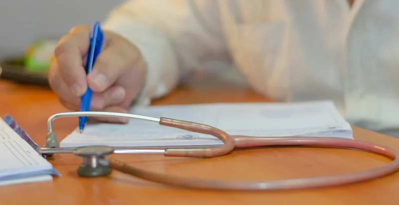 Clinician filling out patient paperwork next to a stethoscope